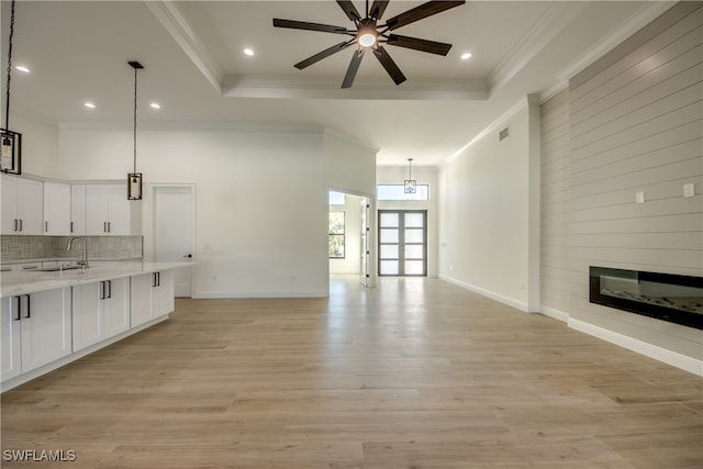 unfurnished living room featuring ceiling fan, light hardwood / wood-style flooring, a raised ceiling, sink, and ornamental molding