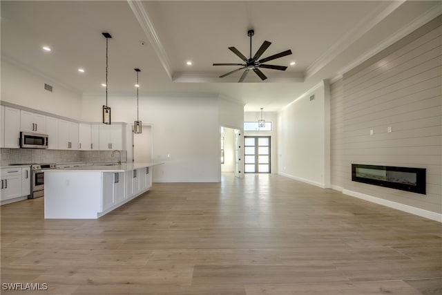 kitchen featuring decorative light fixtures, a center island with sink, appliances with stainless steel finishes, a fireplace, and light wood-type flooring