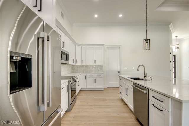 kitchen featuring white cabinets, sink, light hardwood / wood-style flooring, decorative light fixtures, and appliances with stainless steel finishes