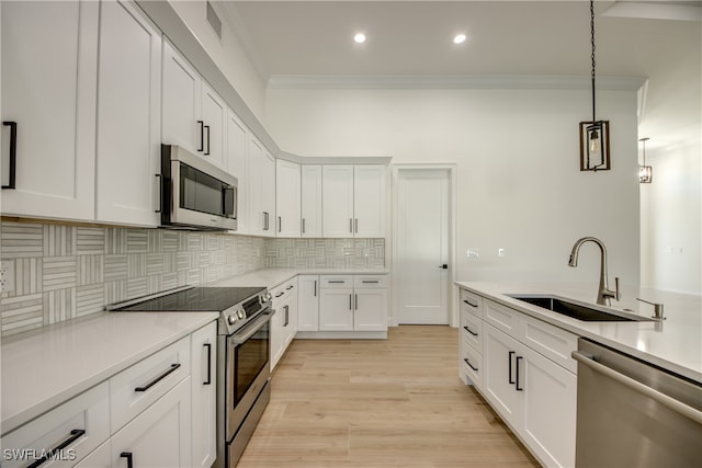 kitchen featuring stainless steel appliances, sink, hanging light fixtures, white cabinetry, and light hardwood / wood-style flooring