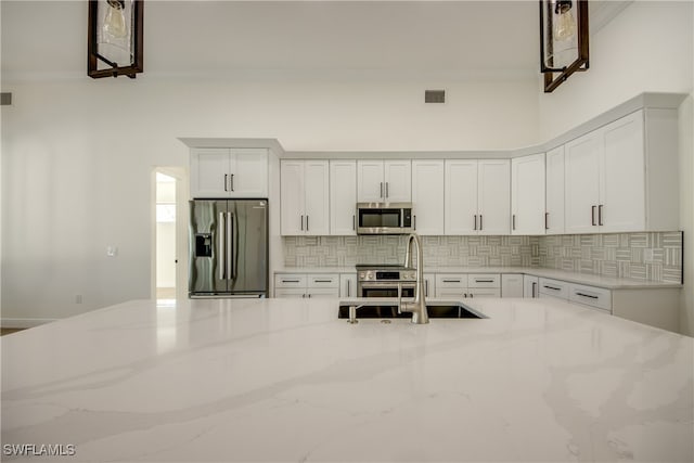 kitchen with white cabinets, sink, tasteful backsplash, stainless steel appliances, and light stone countertops