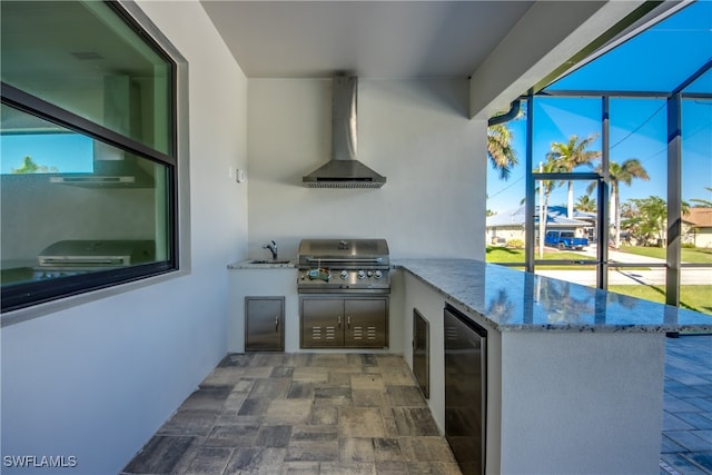 kitchen with light stone countertops, stainless steel fridge, sink, kitchen peninsula, and wall chimney range hood