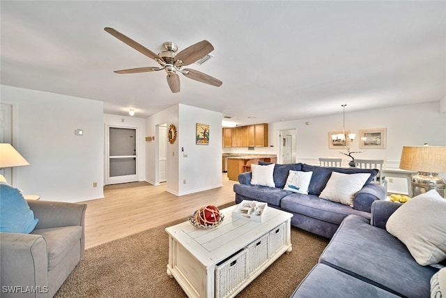 living room with ceiling fan with notable chandelier and light hardwood / wood-style floors