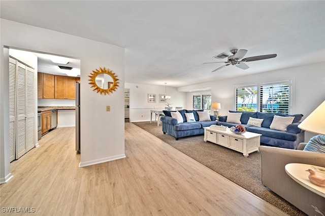 living room featuring ceiling fan with notable chandelier and light wood-type flooring