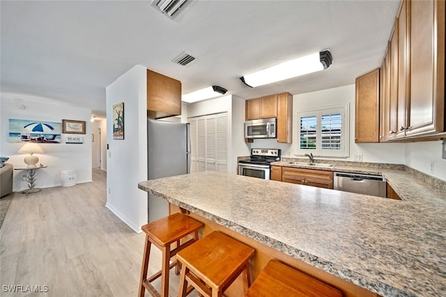 kitchen with light wood-type flooring, a kitchen breakfast bar, sink, stainless steel appliances, and kitchen peninsula