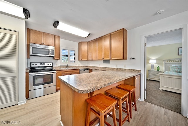 kitchen with kitchen peninsula, sink, appliances with stainless steel finishes, a breakfast bar area, and light wood-type flooring