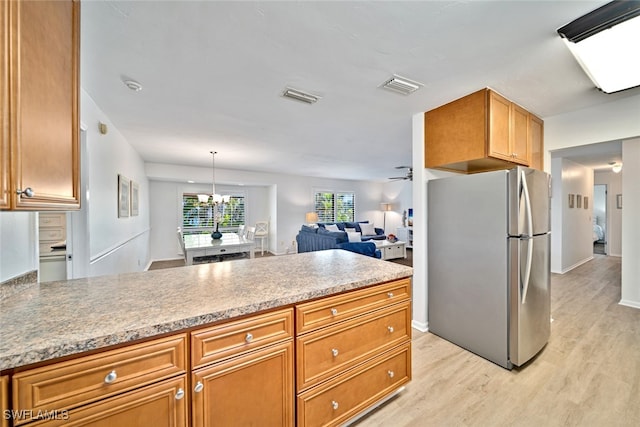 kitchen featuring stainless steel refrigerator, ceiling fan with notable chandelier, light hardwood / wood-style flooring, decorative light fixtures, and light stone counters