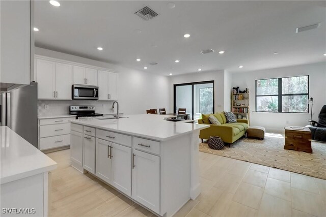 kitchen with tasteful backsplash, stainless steel appliances, sink, white cabinetry, and an island with sink