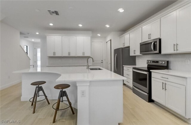 kitchen featuring white cabinets, a kitchen breakfast bar, sink, an island with sink, and appliances with stainless steel finishes