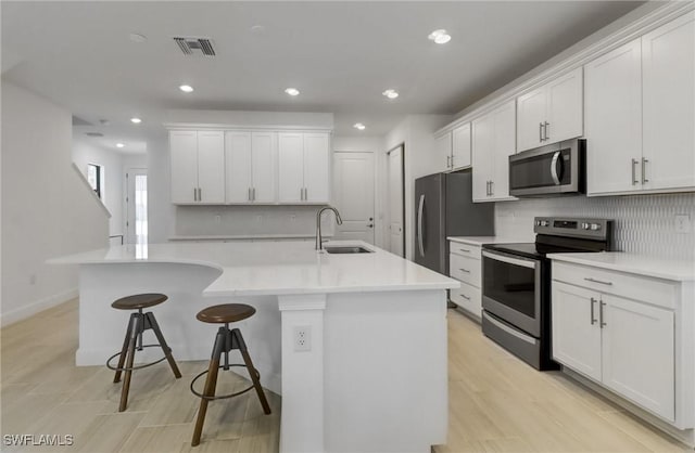 kitchen with visible vents, a breakfast bar, stainless steel appliances, white cabinetry, and a sink