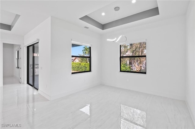 unfurnished room featuring a chandelier, a wealth of natural light, and a tray ceiling