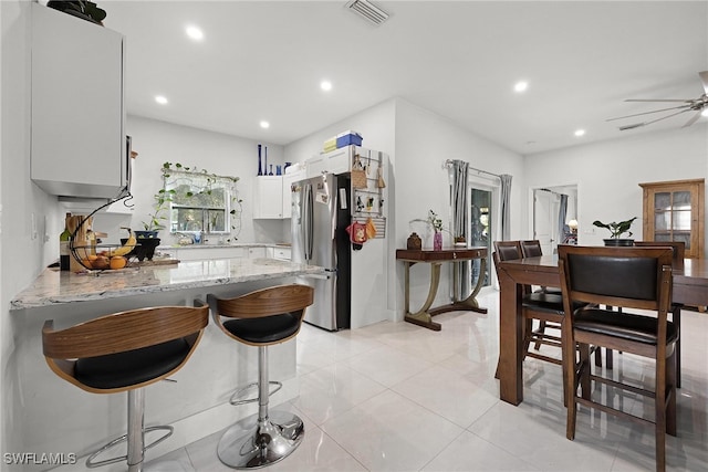 kitchen with kitchen peninsula, stainless steel fridge, a kitchen breakfast bar, white cabinetry, and light stone counters