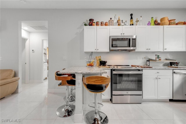 kitchen with a breakfast bar, white cabinets, light stone countertops, and stainless steel appliances