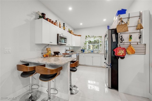 kitchen featuring light stone countertops, appliances with stainless steel finishes, kitchen peninsula, white cabinets, and a breakfast bar area