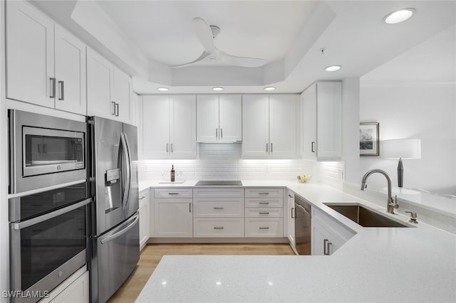 kitchen with white cabinets, stainless steel appliances, a sink, light stone countertops, and decorative backsplash