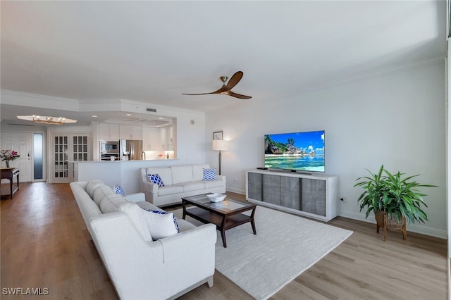 living room with ceiling fan with notable chandelier, ornamental molding, and light hardwood / wood-style flooring