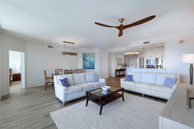 living area featuring light wood-style flooring, baseboards, visible vents, ceiling fan, and ornamental molding