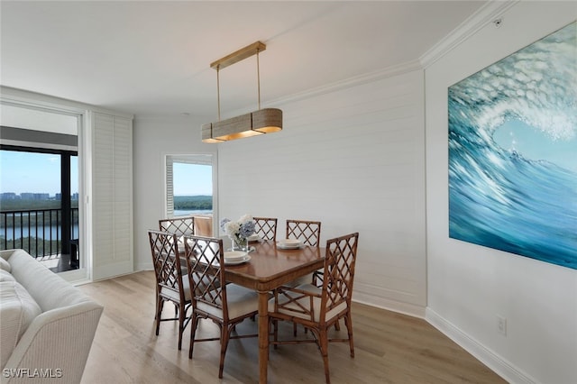 dining space featuring light wood finished floors, baseboards, a water view, and ornamental molding