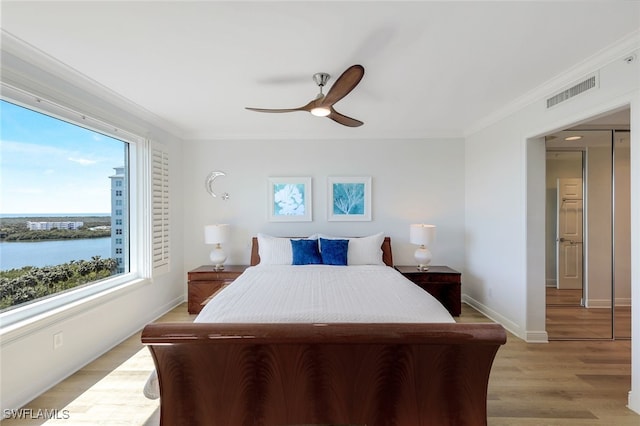 bedroom with ceiling fan, light hardwood / wood-style flooring, ornamental molding, and a water view