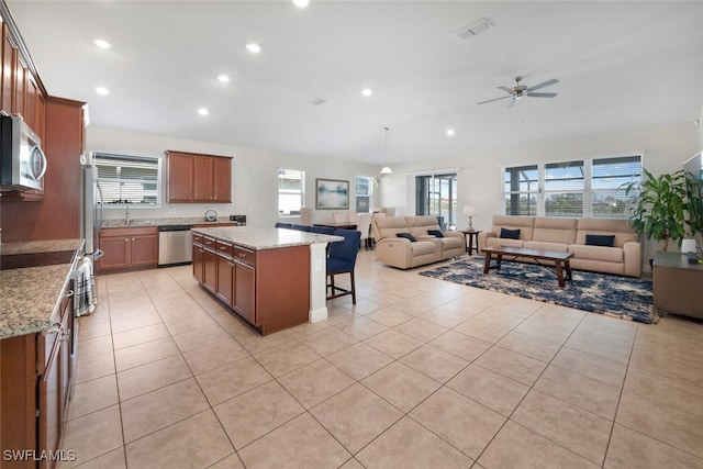 kitchen with light tile patterned floors, a kitchen island, stainless steel appliances, a breakfast bar area, and light stone countertops