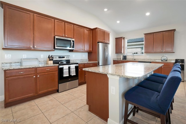 kitchen with light tile patterned flooring, a kitchen island, appliances with stainless steel finishes, a breakfast bar area, and vaulted ceiling