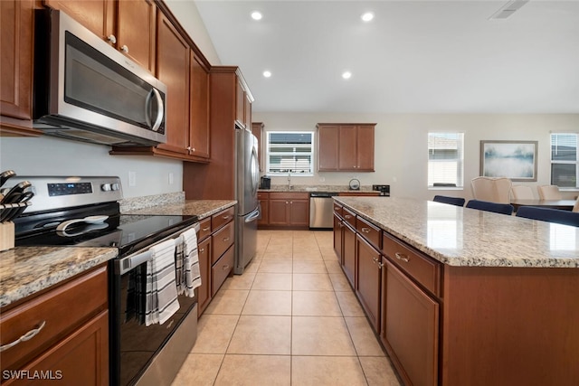 kitchen with stainless steel appliances, light stone countertops, light tile patterned floors, and a center island