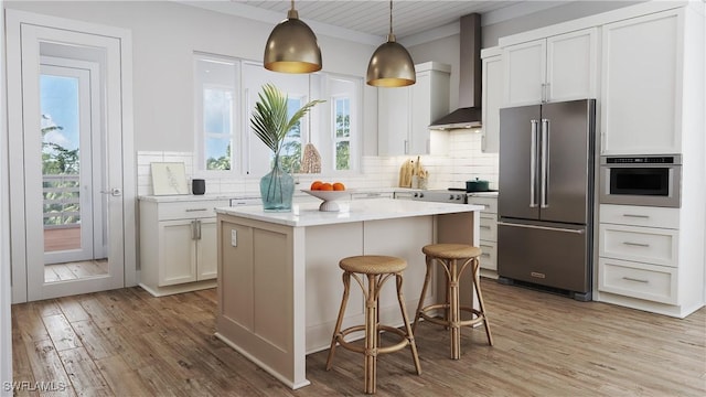 kitchen featuring appliances with stainless steel finishes, white cabinets, a kitchen island, and wall chimney exhaust hood