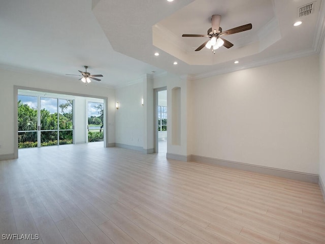 empty room with ceiling fan, light hardwood / wood-style floors, a tray ceiling, and ornamental molding