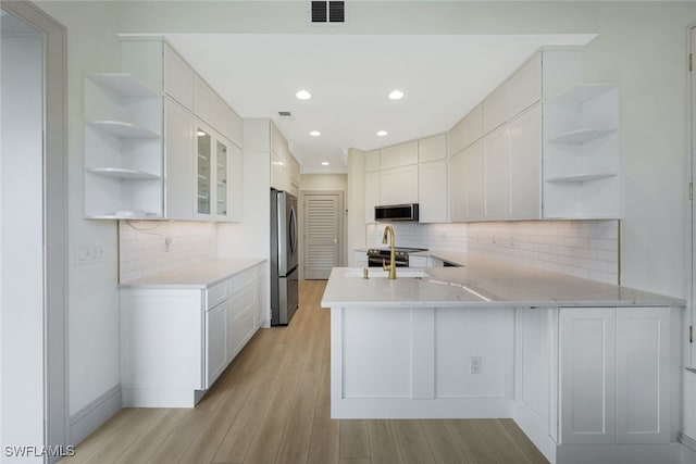 kitchen with appliances with stainless steel finishes, light hardwood / wood-style floors, white cabinets, and kitchen peninsula