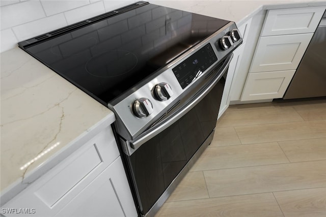 kitchen featuring dishwashing machine, stainless steel range with electric cooktop, light stone counters, and white cabinetry