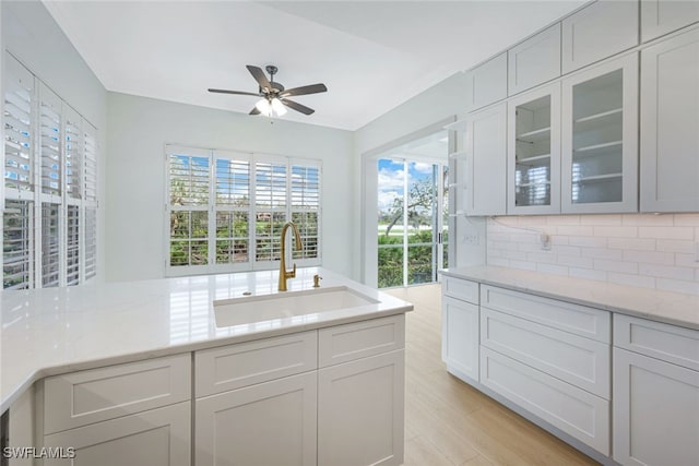 kitchen featuring tasteful backsplash, ceiling fan, sink, light wood-type flooring, and light stone counters