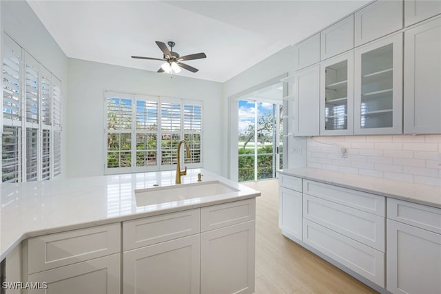26831 Wyndhurst Ct Unit 101, Bonita Springs, FL 34134 - kitchen featuring backsplash, a sink, light stone counters, ceiling fan, and glass insert cabinets