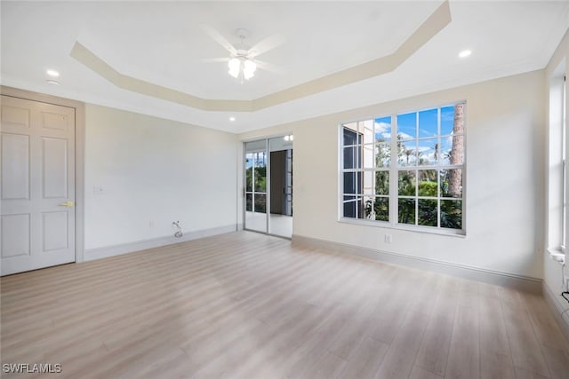 empty room with light wood-type flooring, ceiling fan, and a tray ceiling