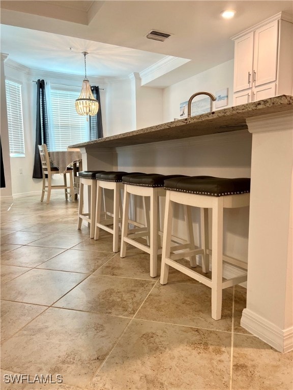 kitchen with a breakfast bar, crown molding, hanging light fixtures, white cabinetry, and stone counters