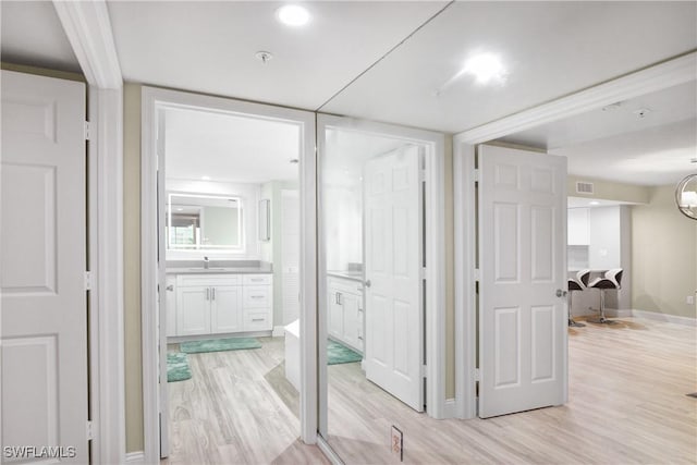 hall with baseboards, visible vents, a sink, and light wood-type flooring