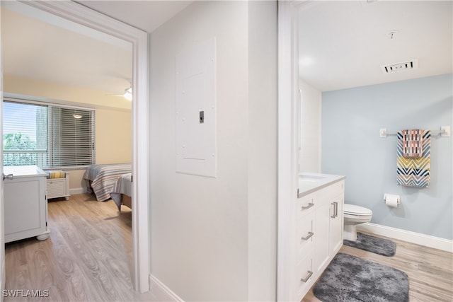 bathroom featuring electric panel, ceiling fan, toilet, wood-type flooring, and vanity