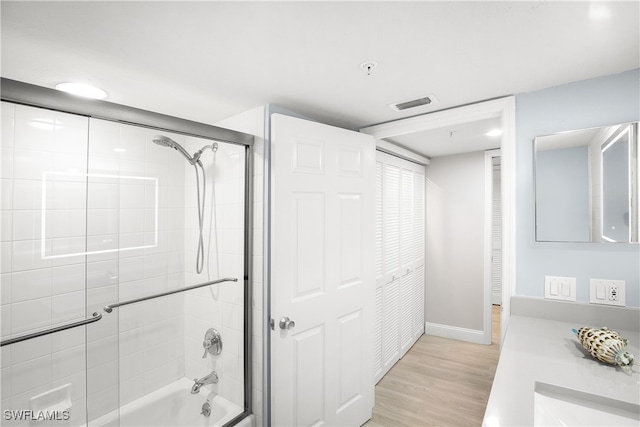 bathroom featuring hardwood / wood-style flooring, vanity, and enclosed tub / shower combo