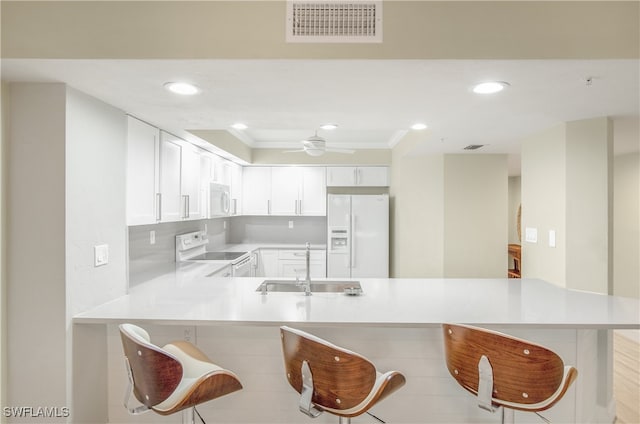 kitchen featuring kitchen peninsula, white appliances, a kitchen breakfast bar, and white cabinets