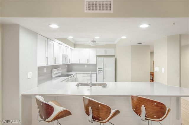 kitchen with a sink, a kitchen bar, white appliances, and visible vents