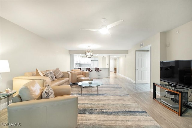 living room with light wood-type flooring, baseboards, ceiling fan with notable chandelier, and visible vents