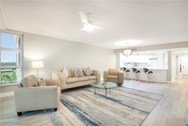 living area with baseboards, visible vents, light wood finished floors, and ceiling fan with notable chandelier