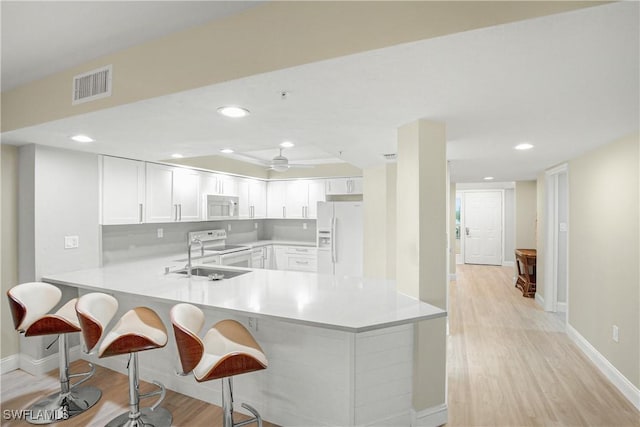 kitchen featuring visible vents, a peninsula, white appliances, a kitchen bar, and a sink
