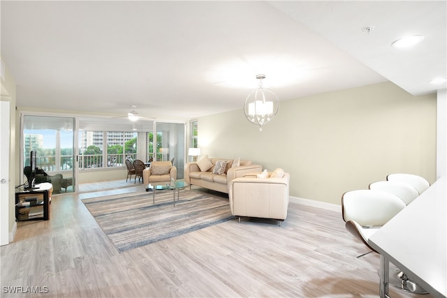 living room featuring ceiling fan with notable chandelier and light hardwood / wood-style flooring