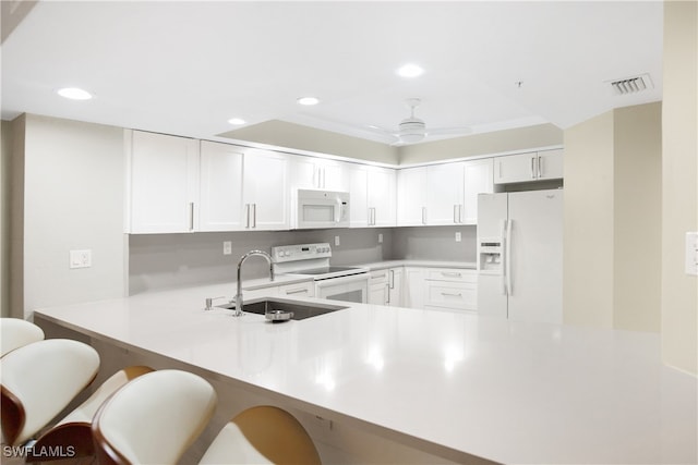 kitchen featuring white appliances, a kitchen breakfast bar, sink, kitchen peninsula, and white cabinets