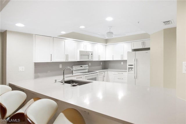 kitchen featuring white appliances, a peninsula, recessed lighting, and a sink
