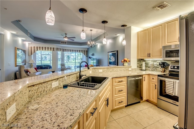 kitchen featuring light stone counters, sink, ceiling fan with notable chandelier, hanging light fixtures, and appliances with stainless steel finishes