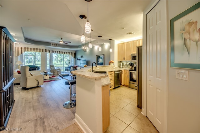 kitchen with ceiling fan, kitchen peninsula, appliances with stainless steel finishes, a breakfast bar area, and light hardwood / wood-style floors