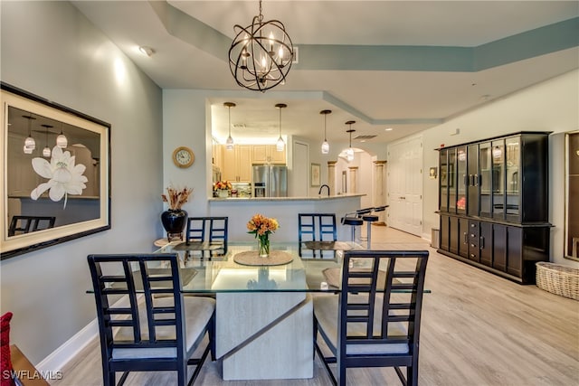 dining space with a tray ceiling, a notable chandelier, light wood-type flooring, and sink