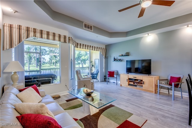 living room featuring ceiling fan, a raised ceiling, and light hardwood / wood-style flooring