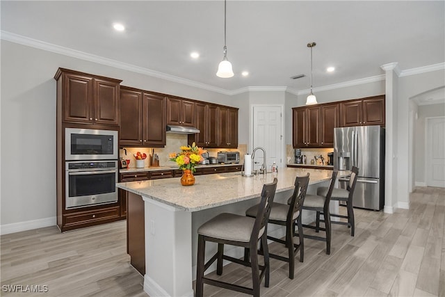 kitchen with appliances with stainless steel finishes, ornamental molding, pendant lighting, a breakfast bar area, and a large island